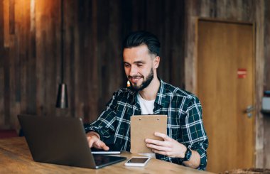 Dizüstü bilgisayarla webinar videosu izleyen mutlu erkek öğrenci ve e-öğrenim ve öğrenim için gülümseme günü, modern netbook 'ta web yayını okuyan evrak işleriyle uğraşan neşeli blogcu