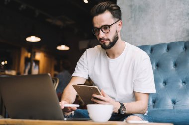Optik gözlüklü beyaz erkek öğrenci dizüstü bilgisayar başında webinar videolar izliyor ve birlikte çalışma alanında öğreniyor. Uzaktan kumandalı ağ teknolojisi üzerinde çalışırken bilgi verici yayınları arayan yetenekli bir adam.