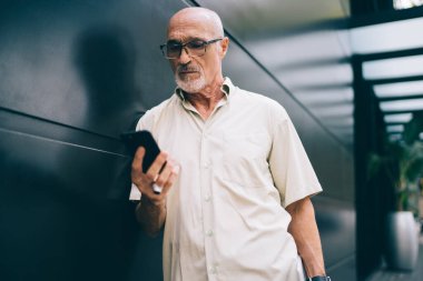 Şehir merkezinde boş zamanlarında alınan e-postaları kontrol etmek için optik göz giysisi içindeki yaşlı beyaz blog yazarı, cep telefonlarını taramak için 4G 'ye bağlanan olgun erkek kullanıcı