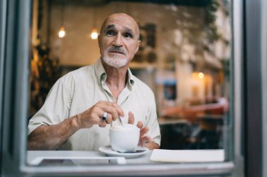 Düşünceli erkek müşteriler, kafenin içinde çay kaşığı ve fincanı tutarak gündüz vakitlerini geçiriyorlar. Kafkasyalı, sıradan gömlekli, düşünceli bir adamın kahve molası sırasında bakışlarını başka yöne çeviriyorlar.