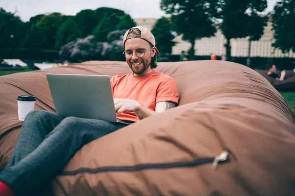 Laughing Optimistic Stylish Guy Baseball Cap Coffee Takeaway Typing Laptop — Stok Foto