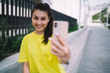 Neşeli Asyalı kadın nüfuzlu biri akıllı telefon kamerasıyla video çekiyor. Şehir caddesinde duruyor, gülümsüyor. Güzel kadın blogcu cep telefonuyla sosyal ağları paylaşmak için fotoğraf çekiyor.