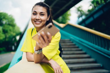 Mutlu kadın merdivenlerde dikiliyor ve cep telefonuna bakıyor. Güneşli bir günde kaldırımda dişlek bir gülümsemeyle.