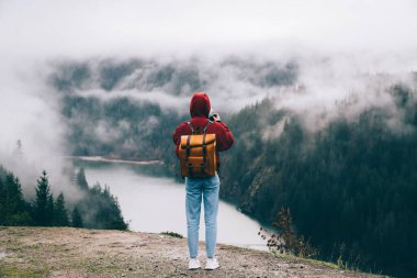Sırtında turuncu bir sırt çantasıyla, puslu bir günde doğayı fotoğraflayan ve doğadaki kayalık bölgede vakit geçiren anonim bir insanın arka planı.