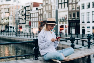 Amsterdam 'da Lotus poz verirken yaz şapkalı, akıllı telefonlu, modaya uygun giyinmiş kadın kaşifin tüm vücudu.