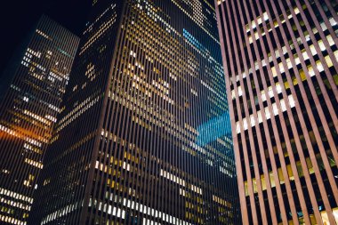 Minimalist metal ve cam gökdelenlerin altından. Gece vakti büyük şehrin merkezinde parlak pencereleri olan.