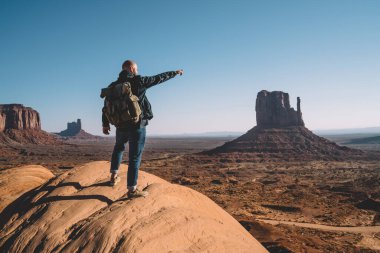 Tam boy tanınmayan günlük kıyafetler ve sırt çantalı bir gezgin kaya üzerinde duruyor ve Anıt Vadisi 'nin resimli manzarasına hayran.