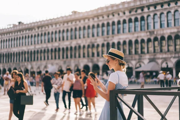 在著名的威尼斯度假期间 穿着盛装站在中世纪建筑附近 一边浏览智能手机的女游客的侧视图 — 图库照片