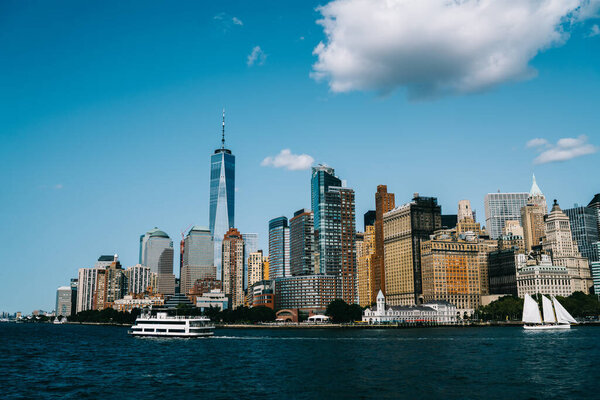 Modern New York waterfront with Manhattan urban skyscrapers in sunny weather with ship and sailing boat passing by in front