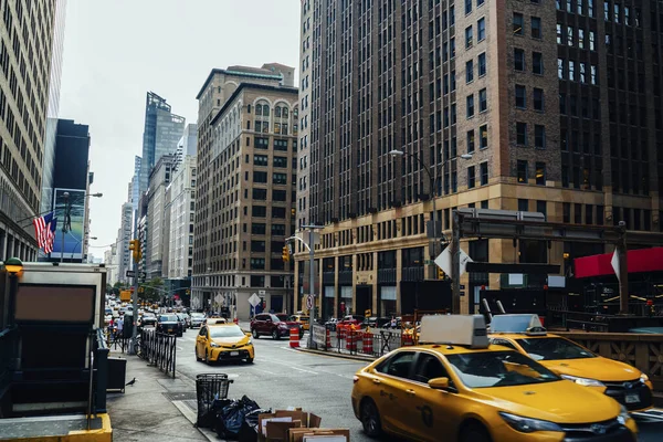 灰色の空に対するアメリカのニューヨーク市の通りに近代的な高層ビルの間のアスファルト道路上のタクシー車 — ストック写真