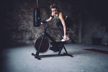 Spor tişörtlü, formda ve kulaklıklı genç bir kadın bisiklet sürmeye hazırlanıyor.