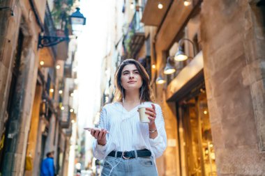 Eski caddede yürürken, kahve içerken ve akıllı telefondan müzik dinlerken neşeli, genç bir bayanın alçak açısı.