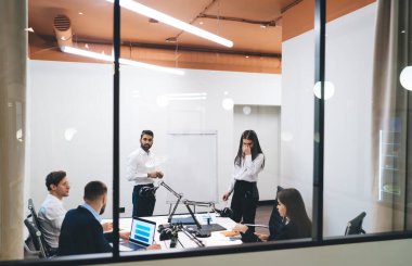 Modern ofis alanında dizüstü bilgisayarlar ve ters çevirme grafikleri kullanarak proje üzerinde çalışan çok ırklı çalışma arkadaşları.