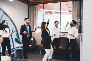 Modern ışık ofisinde duran ve birbirlerine beşlik çakan, resmi giyinmiş bir grup mutlu çok ırklı iş arkadaşı.