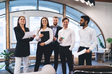 Birlikte başarılı bir toplantı geçirdikten sonra modern ofiste gülümseyen ve ayakta duran, resmi giyinmiş, çok kültürlü meslektaşlardan oluşan neşeli bir grup.