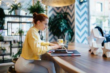 Okul projesi için çevrimiçi araştırma günü için yoğun üniversite öğrencilerinin tavan arası internetine bağlı olduğu bir kenar görüşü, kahve dükkanının ciddi kadın müdürü