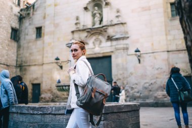 Sırt çantalı genç bir kadın Barselona 'da küçük bir meydanda eski bir çeşmenin yanında yürüyor.