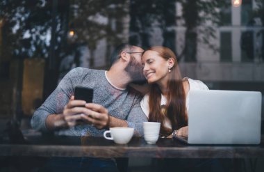 Gündelik giysiler içinde sakallı genç bir adam modern kafede cam arkasında otururken genç bir kadına aşk sözleri fısıldıyor.