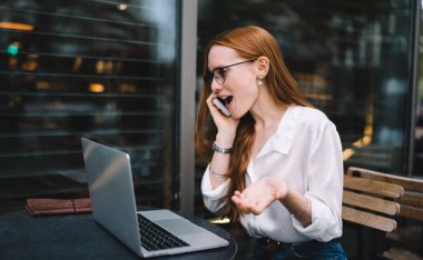 Genç, kızıl saçlı, gözlüklü, hayran bir kadın akıllı telefonla konuşurken ve dizüstü bilgisayarla sokak kafesinde otururken şaşırtıcı haberler alıyor.