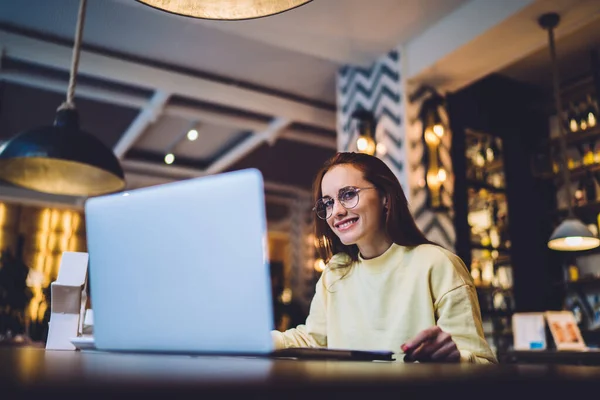 Wesoła Brunetka Freelancer Okularach Żółty Sweter Patrząc Aparat Pracując Laptopie — Zdjęcie stockowe