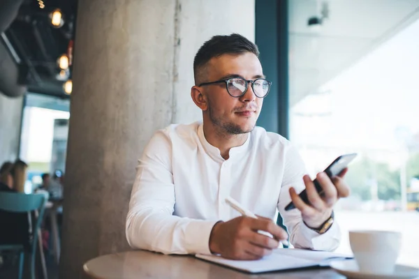 Joven Freelancer Masculino Con Camisa Blanca Anteojos Usando Celular Escribiendo — Foto de Stock