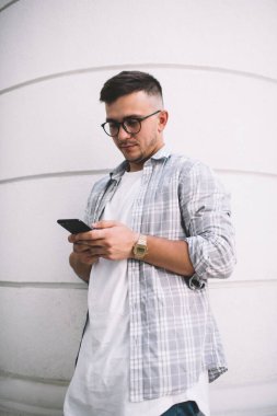 Düşük açılı, bileği ve gözlüklü, beyaz çizgili binaya karşı duran ve gün ışığında sörf yapan sıradan giyinmiş bir adam.