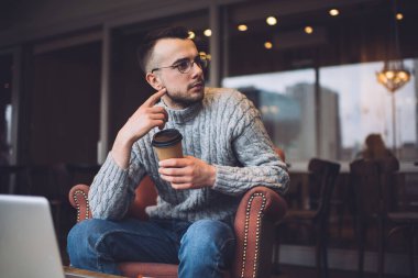 Gri kazaklı ve gözlüklü dalgın bir erkek işten çıkarken modern restoranda dinlenirken başka bir yere bakıyor.