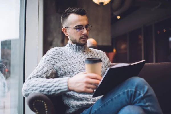 身穿休闲装 头戴眼镜 头戴大胡子的有思想的男性 坐在舒适的扶手椅上 一边喝咖啡 一边看有趣的书 — 图库照片