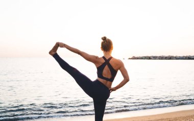 Esnek kadın yogilerin arka görünüşü, Big Toe Poose 'a elini uzatıyor. Kıyı şeridinde sabah antrenmanının keyfini çıkarıyor. Formda kız, denge egzersizi sırasında rahatlamak için akrobik pilates yapıyor.