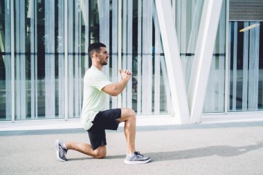 Spor kıyafetleri içindeki atletik erkek sağlıklı yaşam tarzını sürdürüyor. Şehir merkezinde sabahları çömelme egzersizi yapıyor. Vücut konsantrasyonuyla kardiyo aktiviteleri sırasında motive olmuş bir adam.