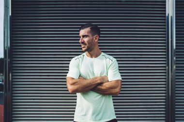 Şehirdeki kentsel ortamların yanında dikilirken ellerini çapraz yapmış kaslı erkek atlet, 30 'lu yaşlardaki beyaz koşucunun sabah vaktini fiziksel dinlenme için harcadığına karar verdi.