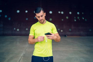 Renkli tişört giyen, elektronik kulaklık ve müzik uygulamalı modern akıllı telefon aygıtı kullanan beyaz erkek koşucu şehir ortamında enerjik kardiyo eğitimi alıyor, sportif yaşam tarzı