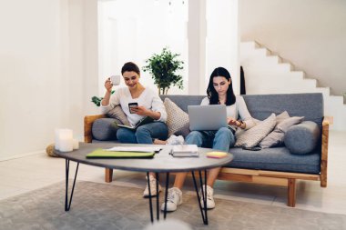 Bir kadın dizüstü bilgisayarla yeni bir proje üzerinde çalışırken diğeri sıcak oturma odasında çay içerken arkadaşlarıyla gülüp sohbet ediyor.