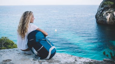 Seyahat sırt çantalı kaygısız kadın kaşif, Menorca adasını ziyaret ederken doğal ortamın tadını çıkarıyor. Sırt çantalı mutlu turist, tek başına kaçarken kayalık görüş açısında dinleniyor.