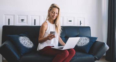 Netbook aygıtı üzerinde çalışırken cep telefonuyla mesajlaşmaktan keyif alan mutlu Kafkasyalı serbest yazar, iletişim uygulaması kurulumu için mobil bildirimi kontrol eden zengin kadın kullanıcı