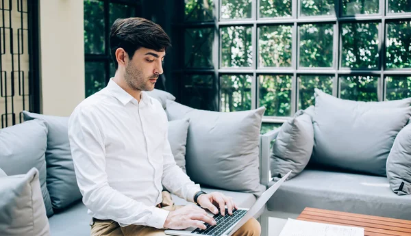 集中的男性企业家穿着正式服装 上网本 坐在沙发上 远程工作的侧视图 — 图库照片