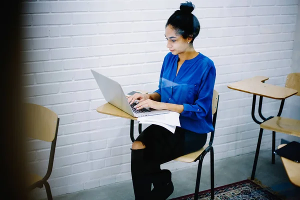 在舒适的大学读书时 穿着休闲装的专注青少年坐在书桌前 坐在上网本旁边 透过玻璃杯 — 图库照片