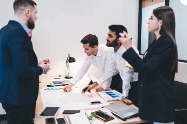 Bir grup etnik çeşitliliğe sahip meslektaşın belge ve akıllı telefonlarla masanın etrafında toplanması ve modern ofis odasındaki iş projesinde beyin fırtınası yapması.