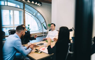 Bir grup neşeli iş arkadaşı resmi giysiler içinde aparatlarla ve kağıtlarla masada otururken aynı zamanda çağdaş ofiste toplanıyorlar.