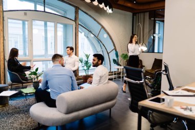 Modern konferans salonundaki rahat koltukları ve geniş pencereleri olan zarif resmi kıyafetli mutlu çok ırklı meslektaşlar proje tartışıyorlar.