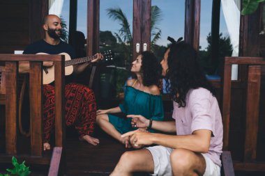 Bir grup mutlu arkadaş terasta oturmuş güneşli günlerde gitar çalarken birlikte vakit geçiriyorlar.
