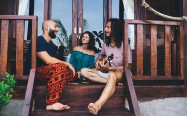 Düşük açılı, çok ırklı, neşeli arkadaşlar. Günlük kıyafetleriyle evin merdivenlerinde oturup birlikte gitar çalıyorlar.