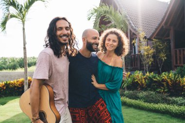 Güneşli bir günde birlikte eğlenirken gündelik giysiler içinde gülümseyen ve gitarla takılan bir grup iyimser arkadaş.