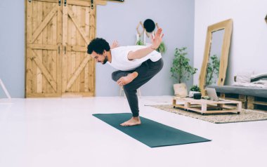 Tişörtlü ve eşofmanlı bir adamın yoga egzersizi yaparken bir bacağının üstünde duran özel duruşu.