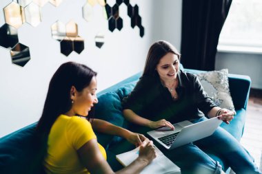 Rahat koltukta oturan ve dizüstü bilgisayarları karıştıran gündelik giyinen pozitif kadınların yüksek açısı.