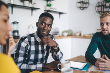 Konsantre genç erkek çalışanlar, modern çalışma alanında iş konuşurken masada oturup kadın meslektaşlarını dikkatle dinliyorlar.