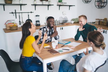 Bir grup çok ırklı genç iş arkadaşı, rahat çalışma ortamında tablet ve not defterleriyle iş projesinde çalışırken günlük giysiler içinde konuşuyor ve gülüyorlar.