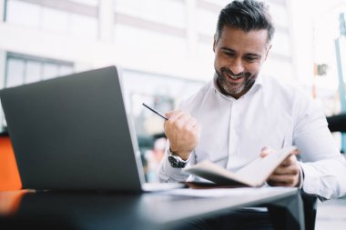 Heyecanlı 40 'lı yaşlardaki beyaz gömlekli girişimci, iş sonuçlarından memnun, kişisel planlamacı ile mutlu beyaz erkek CEO' su netbook 'la kaldırım kenarında oturan hedefini kutluyor.