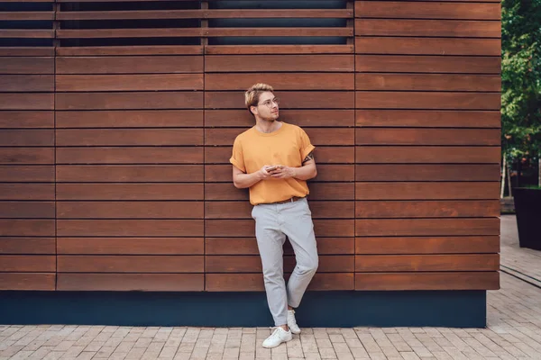 Young Guy Orange Shirt Light Grey Pants Leaning Back Wooden — Stock Photo, Image