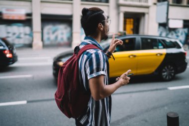 Afrika kökenli Amerikalı hippi adam Megalopolis caddesinde taksiye biniyor, koyu tenli turist bulvarda hareketli şehir trafiğine bakıyor ve araçları durduruyor.